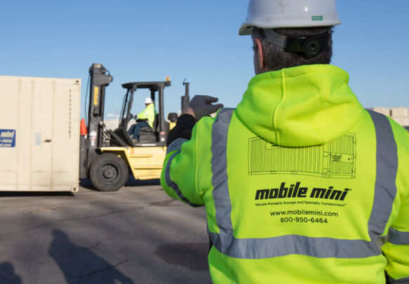 A Mobile Mini employee instructing a forklift to move a container.